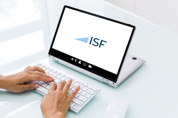 Ein Laptop mit ISF Logo auf einem Glastisch. Davor eine Tastertur mit Händen die tippen.